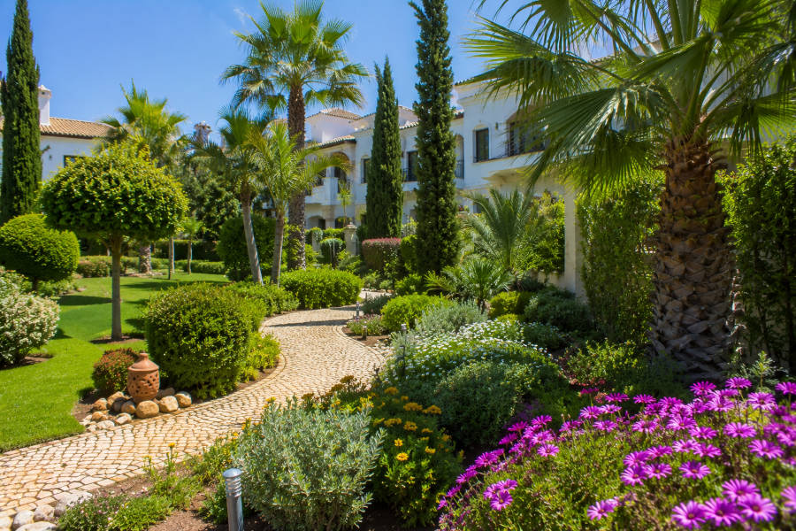 Um belo jardim com flores, palmeiras, árvores e um caminho num hotel em Portimão